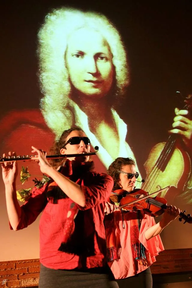 Deux musiciennes sur scène, à la flûte traversière et au violon, devant un grand portrait projeté de Vivaldi.