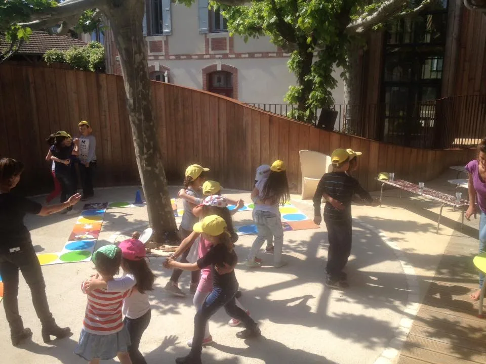Des enfants jouent au jeu de l'oie géant en plein air, dans une cour d'école.